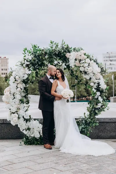 Büyük şehirde çiçek kemerinin arka planında güzel bir düğün çifti.