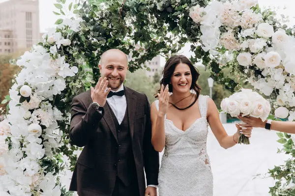 Mutlu yeni evliler gelin ve damat yüzüklerini gösterip şehirde poz veriyorlar.