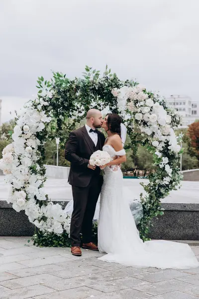 Çiçek kemerinin yanında öpüşen genç bir çift.