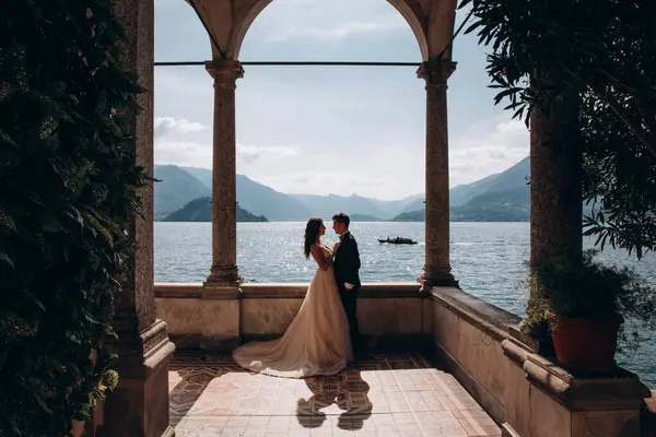 Mutlu genç gelin ve damat gölün ve dağların arkasında poz veriyor.