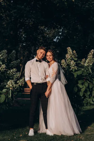 Mutlu gelin ve damat el ele tutuşup parkta kameraya gülümsüyor.