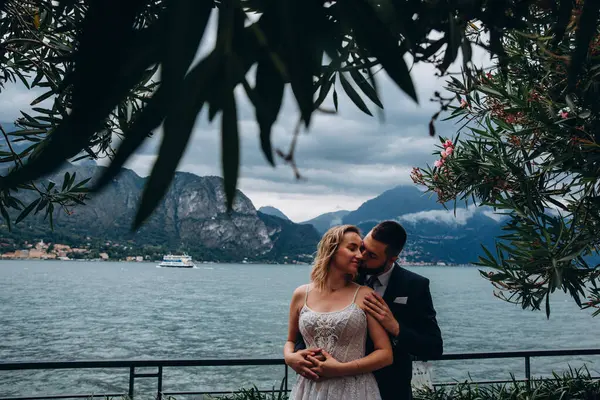 Mutlu çift göl kenarındaki dağlarda sarılıp öpüşüyor.