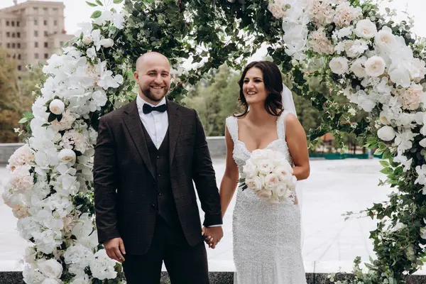 Mutlu gelin ve damat düğün gününde el ele tutuşup gülümsüyor.