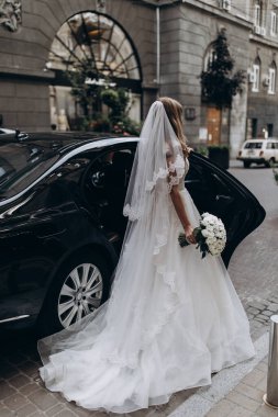 zarif beyaz gelinlikli gelin sokakta arabanın yanında poz veriyor.