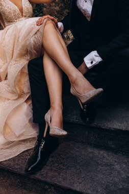 Lüks elbiseli güzel bir gelin ve merdivenlerde oturan damatlı ayakkabılar.