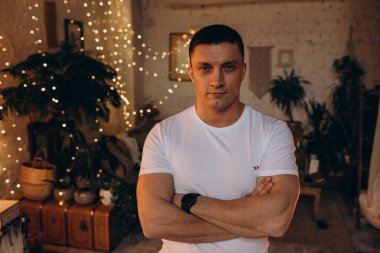 Kollarını kavuşturup, rahat bir şekilde kameraya bakan yakışıklı bir gencin portresi.  