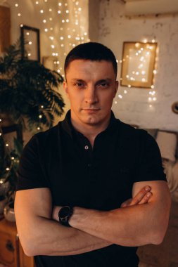 Kollarını kavuşturup, rahat bir şekilde kameraya bakan yakışıklı bir gencin portresi.  