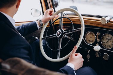 Eski model araba kullanan takım elbiseli bir adamın kırpılmış görüntüsü.