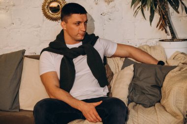 Kanepede otururken stüdyoda poz veren genç yakışıklı adam.