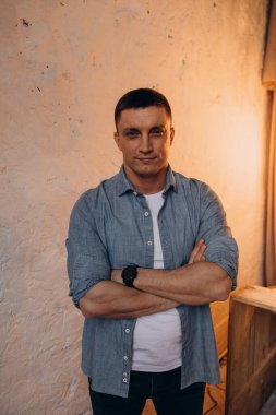 Stüdyoda kollarını kavuşturmuş sıradan giyinmiş bir adamın portresi. 