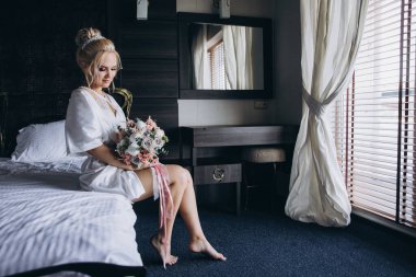 Güzel genç gelin düğün sabahı zarif iç kısımlarında çiçek buketi tutuyor.                      