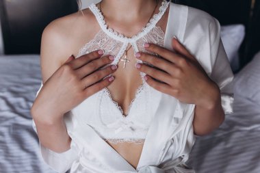 Beyaz iç çamaşırlı kadın yatakta beyaz çarşaf üzerinde poz veriyor. 