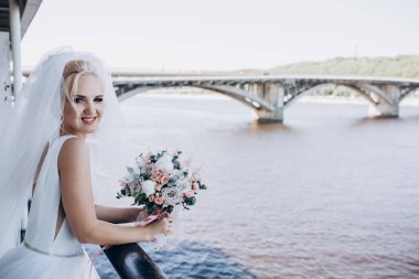 Nehir ve köprünün arka planında buket olan gelinlik içinde güzel bir gelin..  