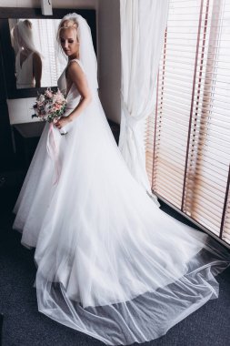 Güzel genç gelin düğün sabahı zarif iç kısımlarında çiçek buketi tutuyor.                      