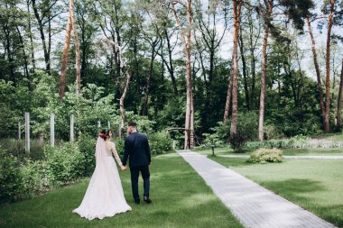 Gelinlikli güzel bir gelin ve parkta yürüyen yakışıklı bir damat..