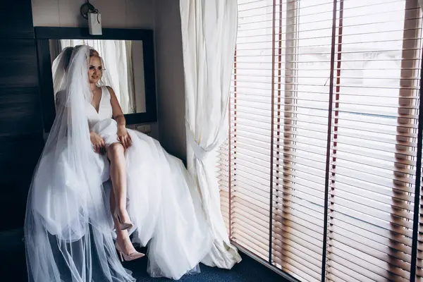 Güzel, mutlu, gelinlikli gelin rahat bir odada oturuyor.