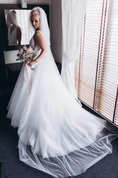 Güzel genç gelin düğün sabahı zarif iç kısımlarında çiçek buketi tutuyor.                      