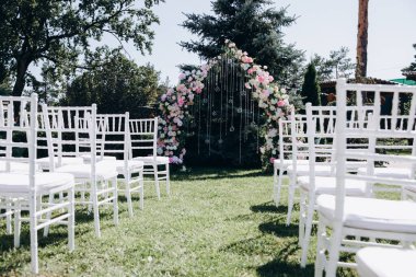 Çiçekli kemer ve sandalyeli bahçede düğün töreni. 