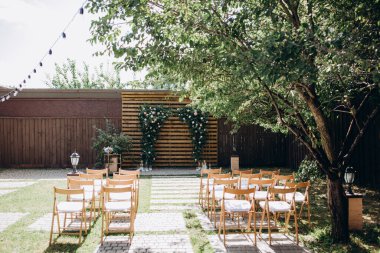 Çiçekli kemer ve sandalyeli bahçede düğün töreni. 