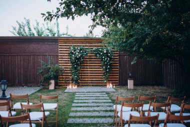 Çiçekli kemer ve sandalyeli bahçede düğün töreni. 