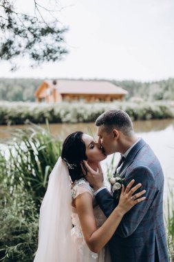 Güzel gelin ve damat düğün günlerinde göl kenarında öpüşürler.