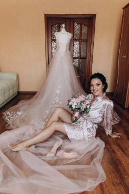 Mutlu genç gelin elinde buket ve zarif elbisenin yanında oturuyor.