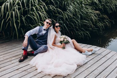 Düğün çifti göletin yanındaki ahşap iskelede oturuyor..