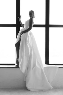 Beyaz gelinlikli güzel sarışın gelinin portresi. Evdeki pencere pervazında poz veriyor.                            