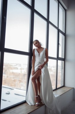 Beyaz gelinlikli güzel sarışın gelinin portresi. Evdeki pencere pervazında poz veriyor.                            