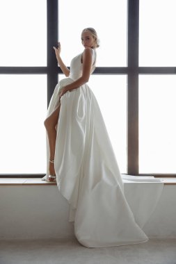 Beyaz gelinlikli güzel sarışın gelinin portresi. Evdeki pencere pervazında poz veriyor.                            