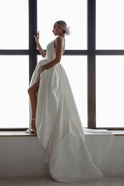 Beyaz gelinlikli güzel sarışın gelinin portresi. Evdeki pencere pervazında poz veriyor.                            