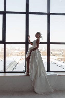 Beyaz gelinlikli güzel sarışın gelinin portresi. Evdeki pencere pervazında poz veriyor.                            