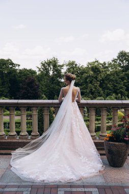 Gelinlik giymiş güzel gelinin terasta dikilip parka bakışının arkası. 
