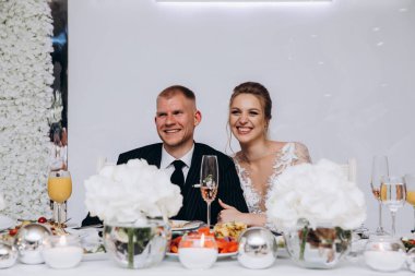 Güzel genç gelin ve damat birlikte restoranda oturuyor ve gülümsüyor.