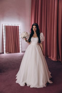 Zarif gelinlik içinde güzel bir buket çiçek taşıyan çekici bir gelinin portresi.                      