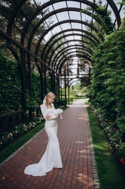 Genç mutlu sarışın gelin parkta gelinlik içinde poz veriyor.