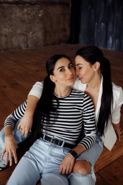 Mutlu genç kadınlar birlikte oturuyor ve stüdyoda poz veriyorlar.