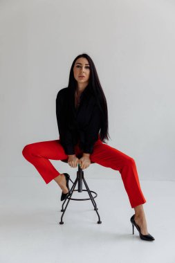 Gri arka planda, sandalyede oturan çekici esmer kadının tüm vücudu.