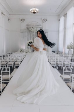 Zarif gelinlik içinde güzel bir buket çiçek taşıyan çekici bir gelinin portresi.                      