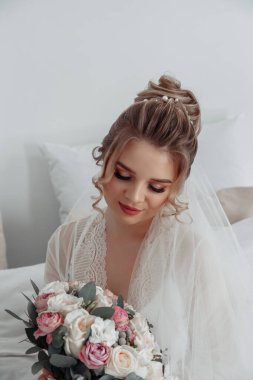 Duvak takmış genç bir gelin. Yatağında bir buket çiçek tutuyor..        