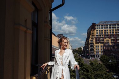 Beyaz cüppeli, duvak takmış, şehirde balkonda poz veren çekici bir gelin.            