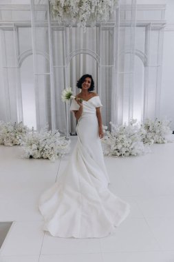 Zarif gelinlik içinde güzel bir buket çiçek taşıyan çekici bir gelinin portresi.                      