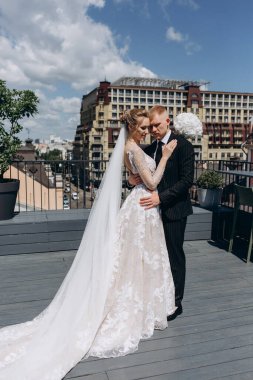 Güzel, mutlu gelin ve damat şehirde terasta sarılıyor.