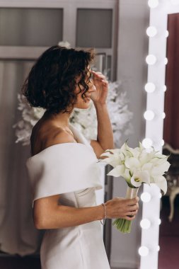 Zarif gelinlik içinde güzel bir buket çiçek taşıyan çekici bir gelinin portresi.                      