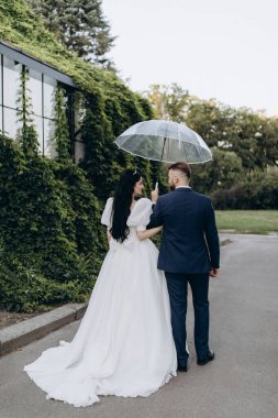 Parkta şemsiyeli gelin ve damadın arka manzarası