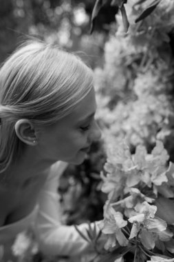 Genç ve güzel bir kadın parkta bahar çiçeklerine bakıyor, siyah ve beyaz.