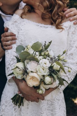 Genç bir çift kucaklaşıyor, gelin buketi tutuyor.