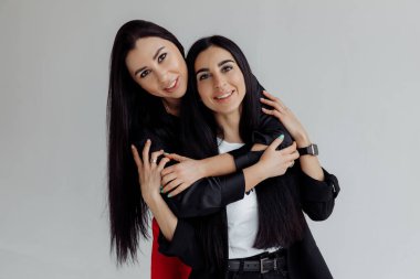 Gri arka planda poz veren siyah elbiseli iki kadın.