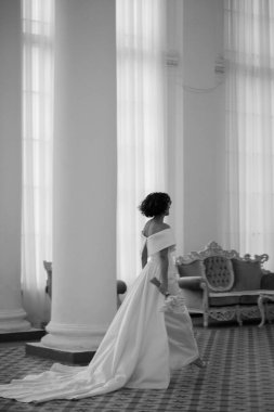 Beyaz elbiseli güzel gelin elinde buket ve düğün salonunda yürüyor.