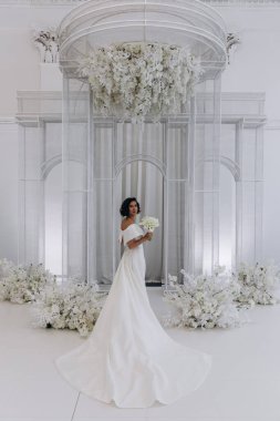 Çekici, mutlu, gelinlik içinde, elinde bir buket çiçek tutan genç gelin.            